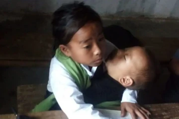 தனது தங்கையை மடியில் சுமந்தபடி பாடம் படிக்கும் 10 வயது சிறுமி!